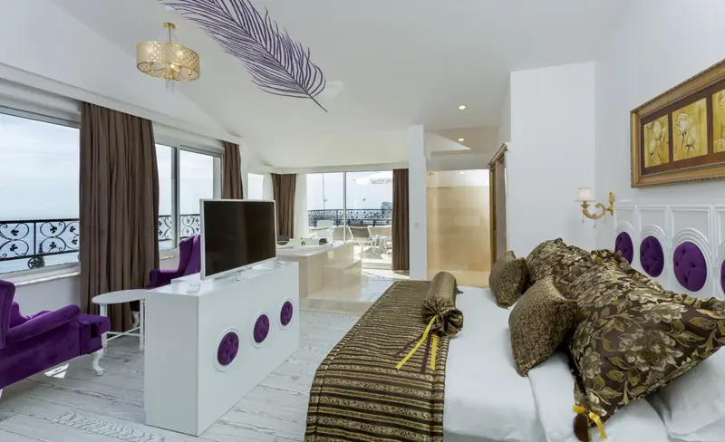 Eine Suite mit Meerblick: ein Doppelbett, eine Sitzecke mit Sesseln und eine Terrasse mit Wanne hinter den Schiebetüren.