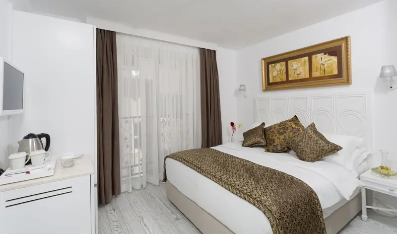 Ein Standard-Doppelzimmer: ein Doppelbett, ein Wandfernseher, ein Wasserkocher mit Tee- und Kaffeetablett und ein französischer Balkon mit Vorhängen.