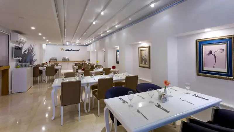 Das Hotelrestaurant, in dem das Frühstück serviert wird: weiße Tische mit Gläsern und Besteck, im Hintergrund ein Buffet.